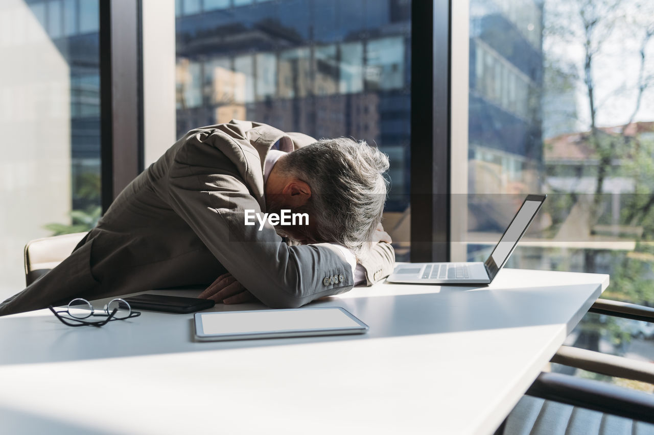 Tired businessman sitting at desk by window in office