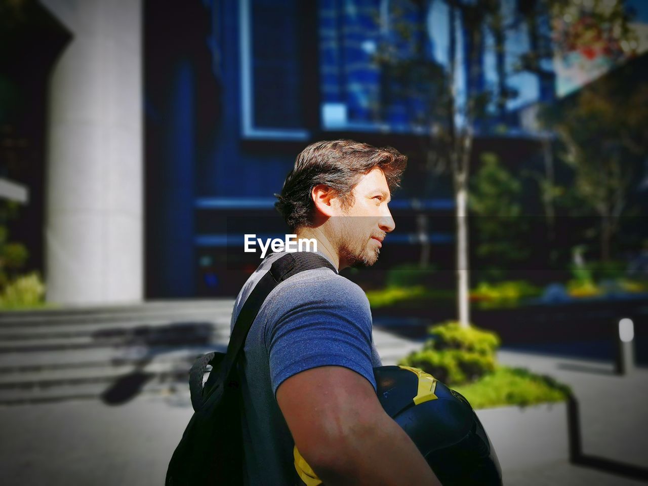 Side view of man looking away while standing with bag against building