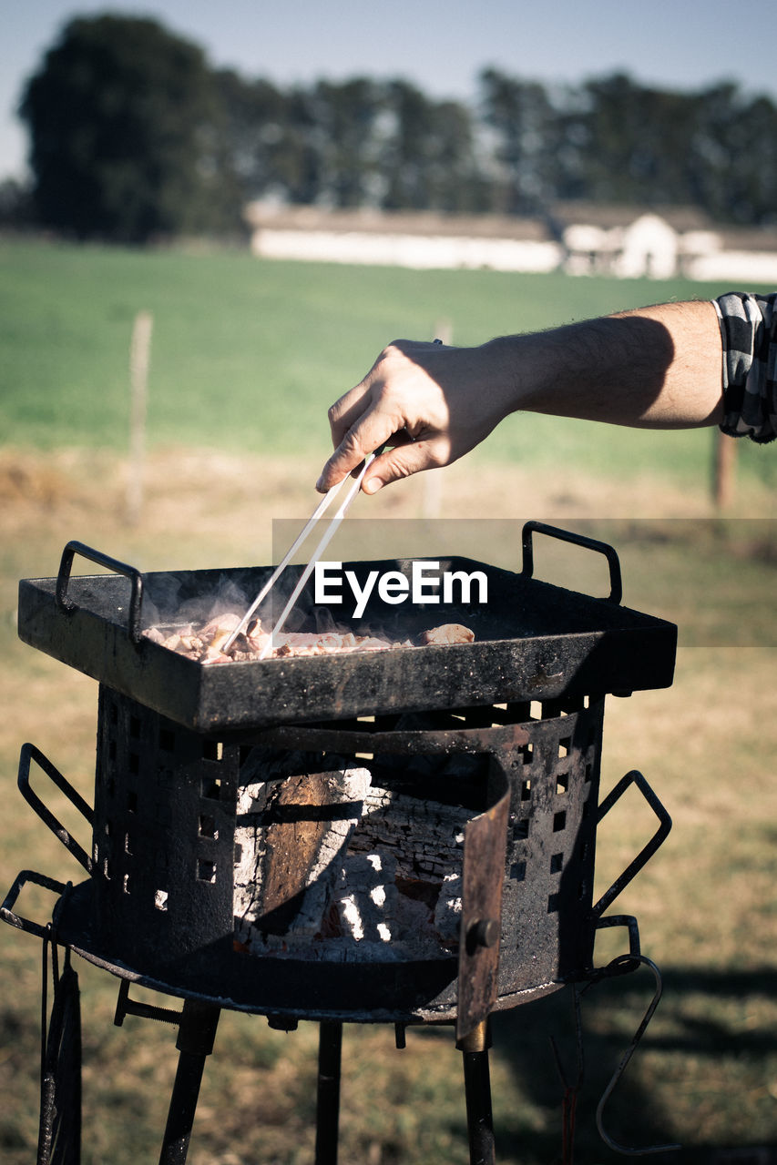 Man preparing food on barbecue grill at field