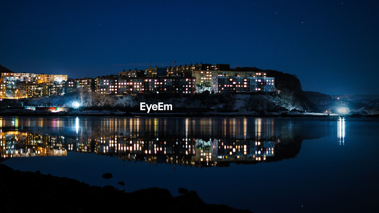 Illuminated cityscape by sea against clear blue sky at night