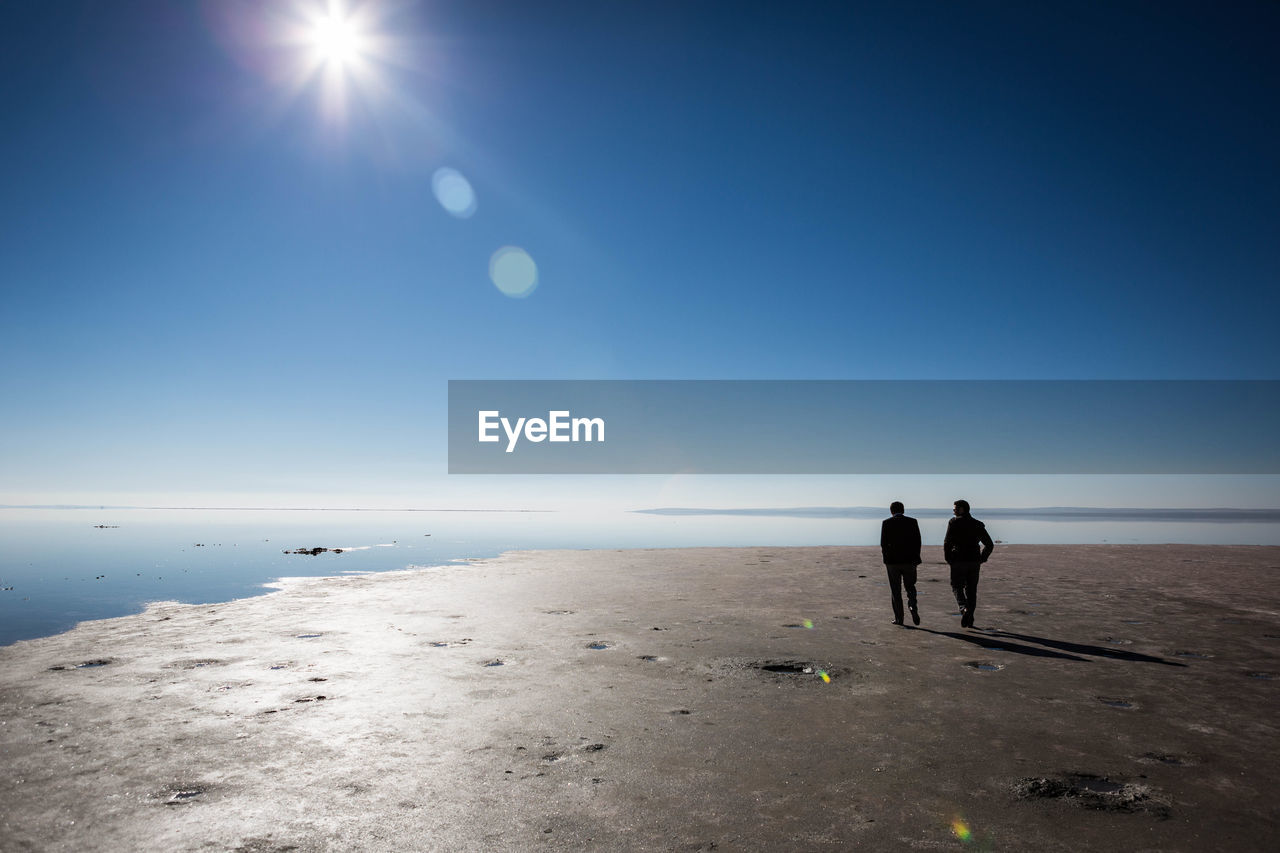 Rear view of two men walking on beach