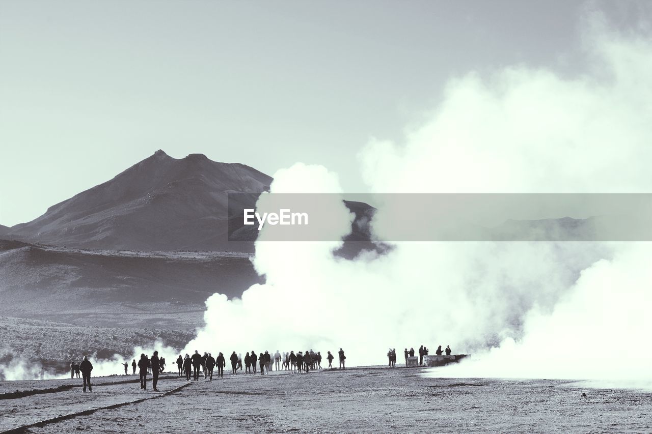 View of people by smoke emitting from geyser against sky