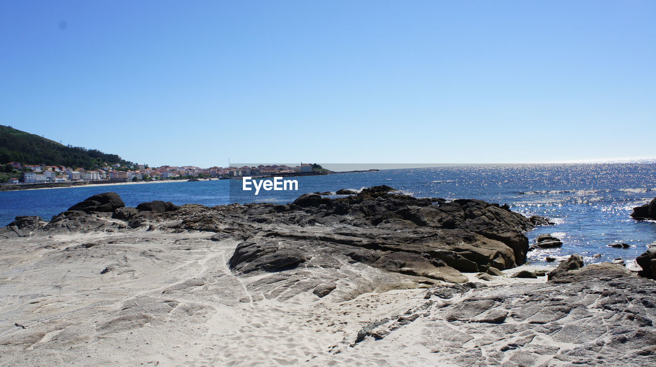 Scenic view of sea and rocky beach against clear sky