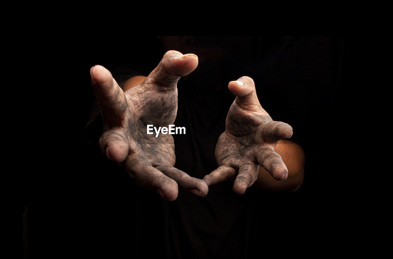 Close-up of messy hands gesturing against black background