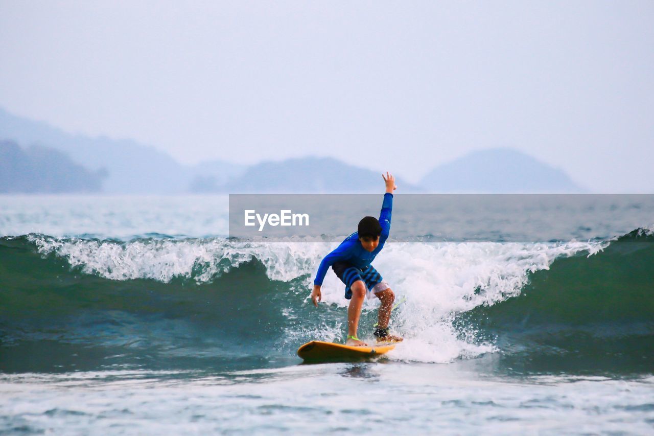 Full length of boy surfing on sea against sky