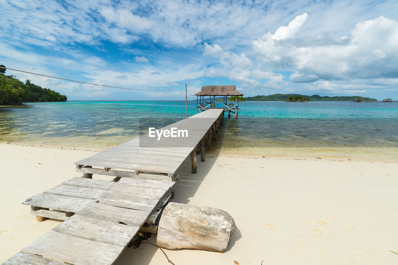 Wooden pier at beach against cloudy sky