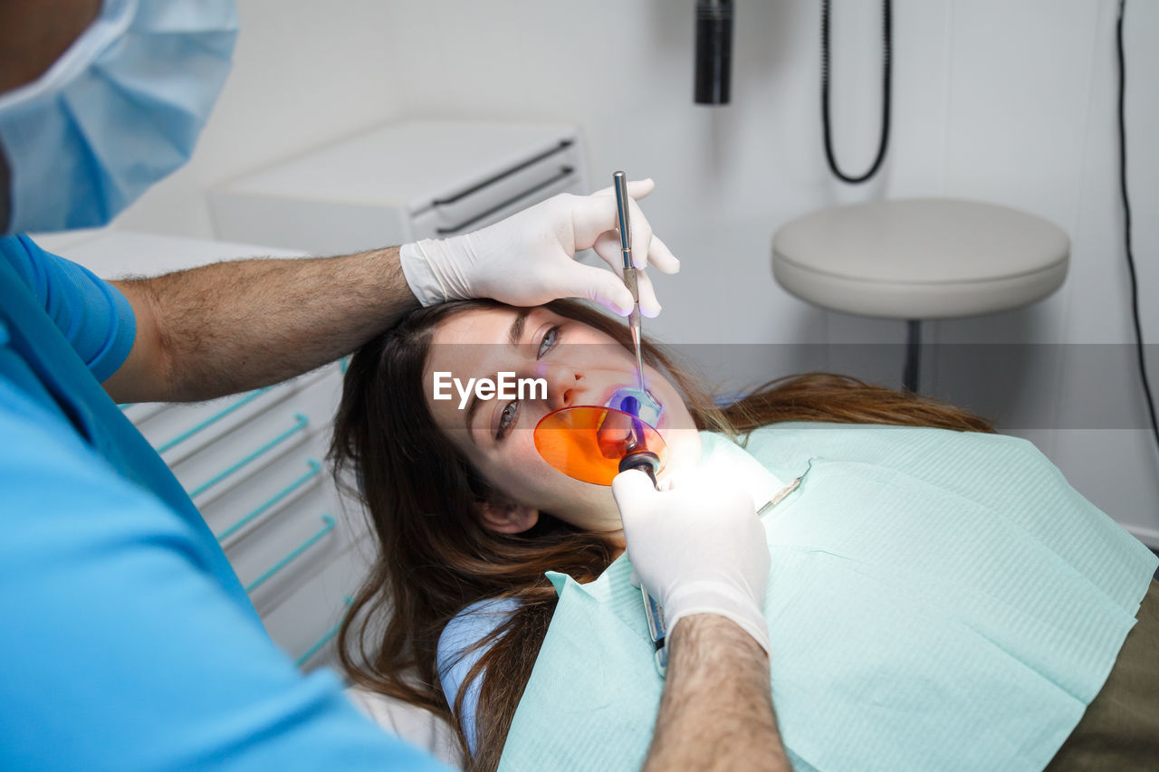 Midsection of male dentist treating female patient in clinic