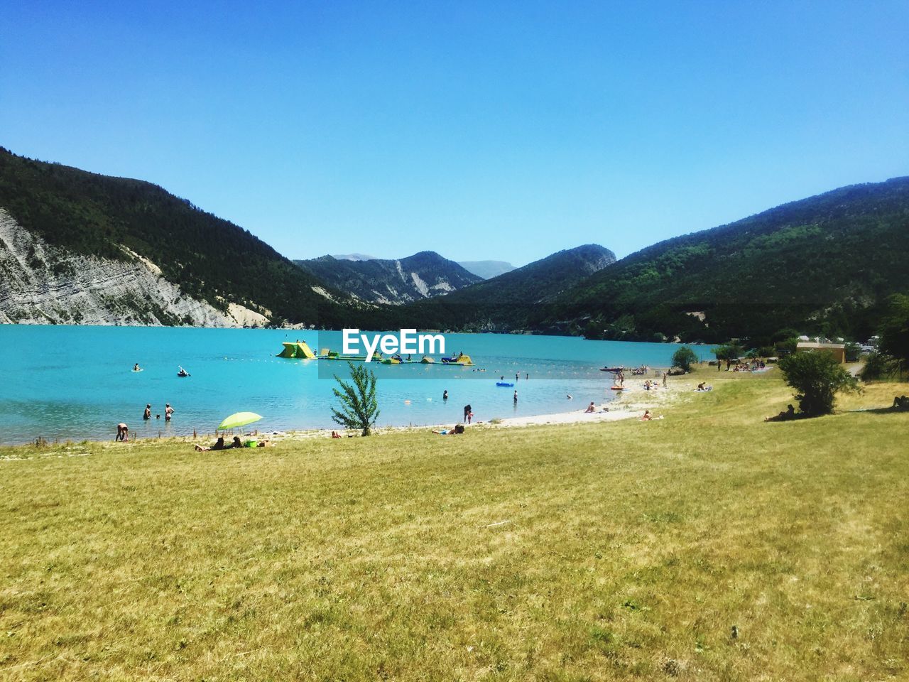SCENIC VIEW OF PEOPLE ON MOUNTAIN BY SEA AGAINST CLEAR BLUE SKY