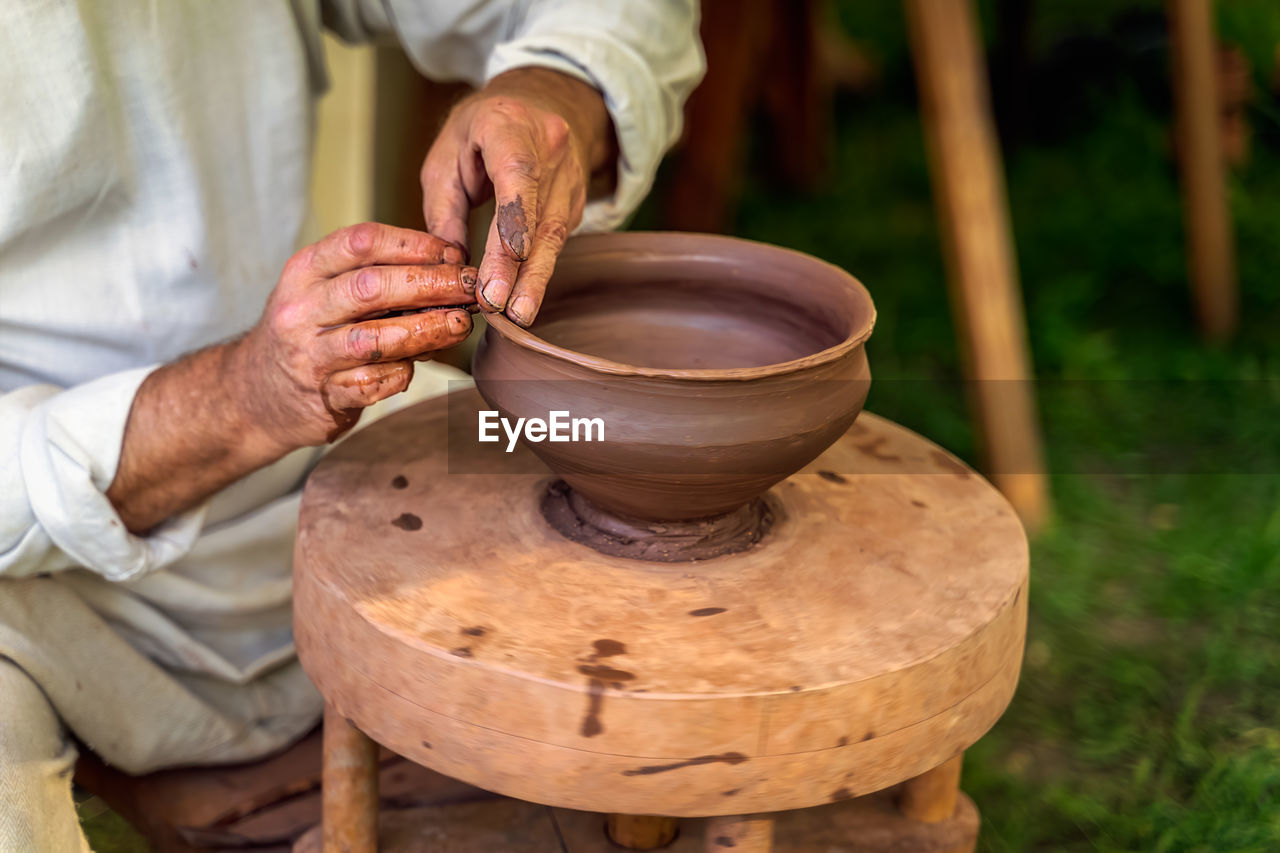 Midsection of man molding shape of pot on potters wheel