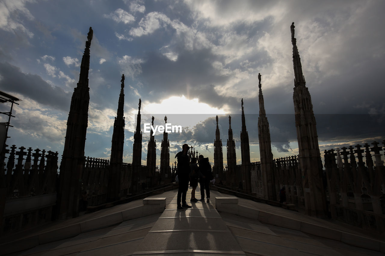 Silhouette people on pathway against clouds