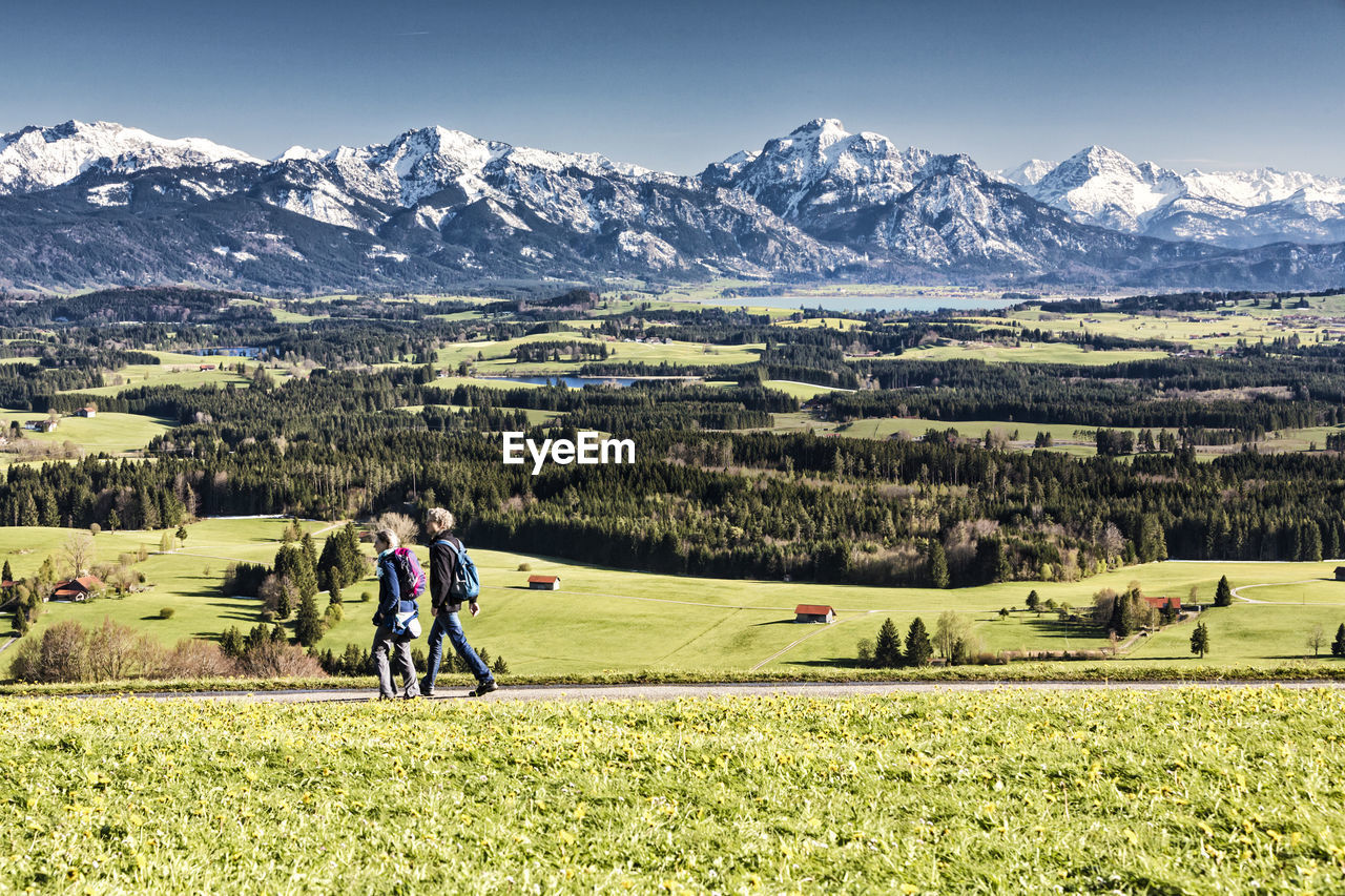 People walking amidst field against mountains