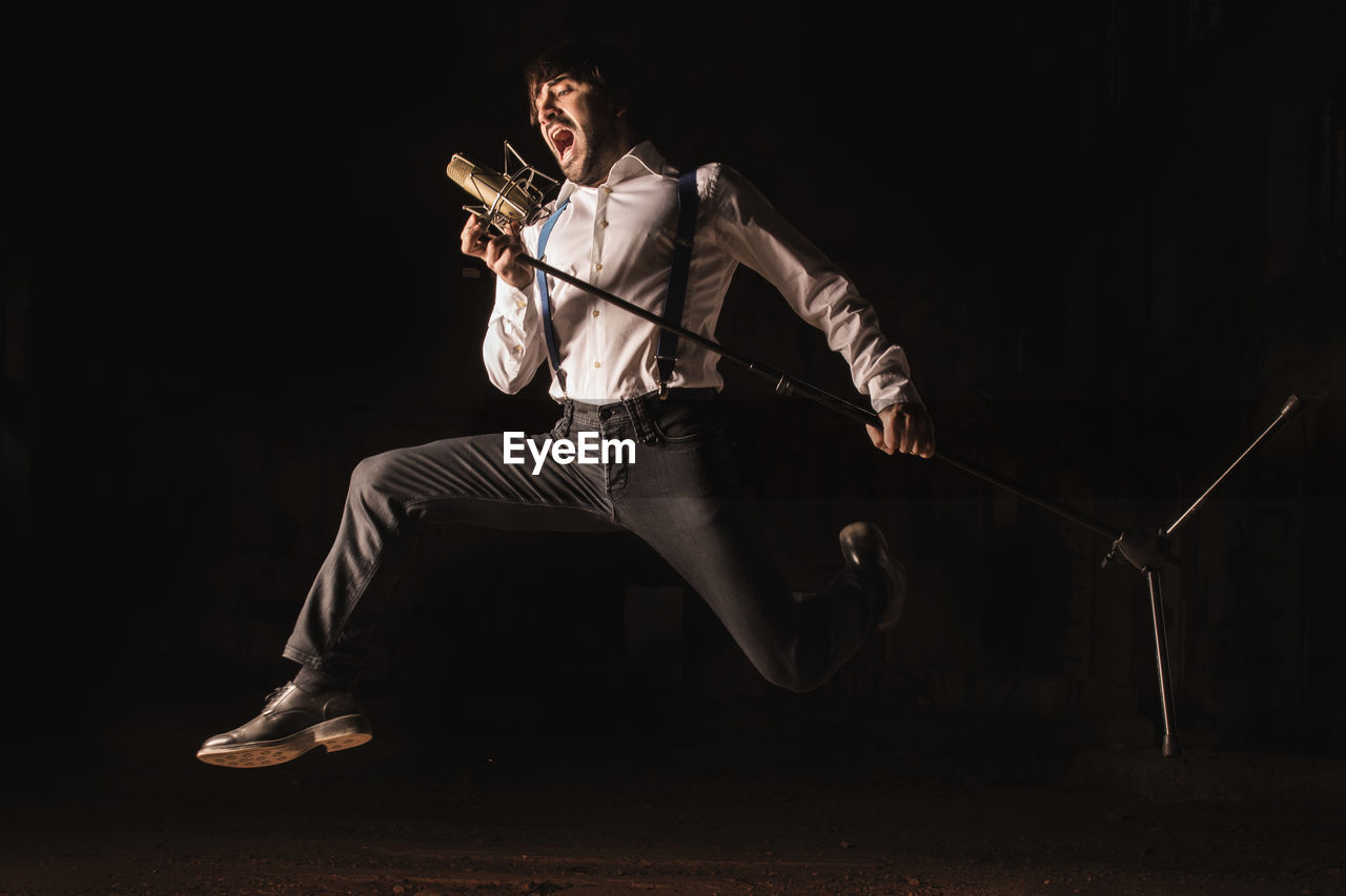 Full length of man singing while holding microphone over black background