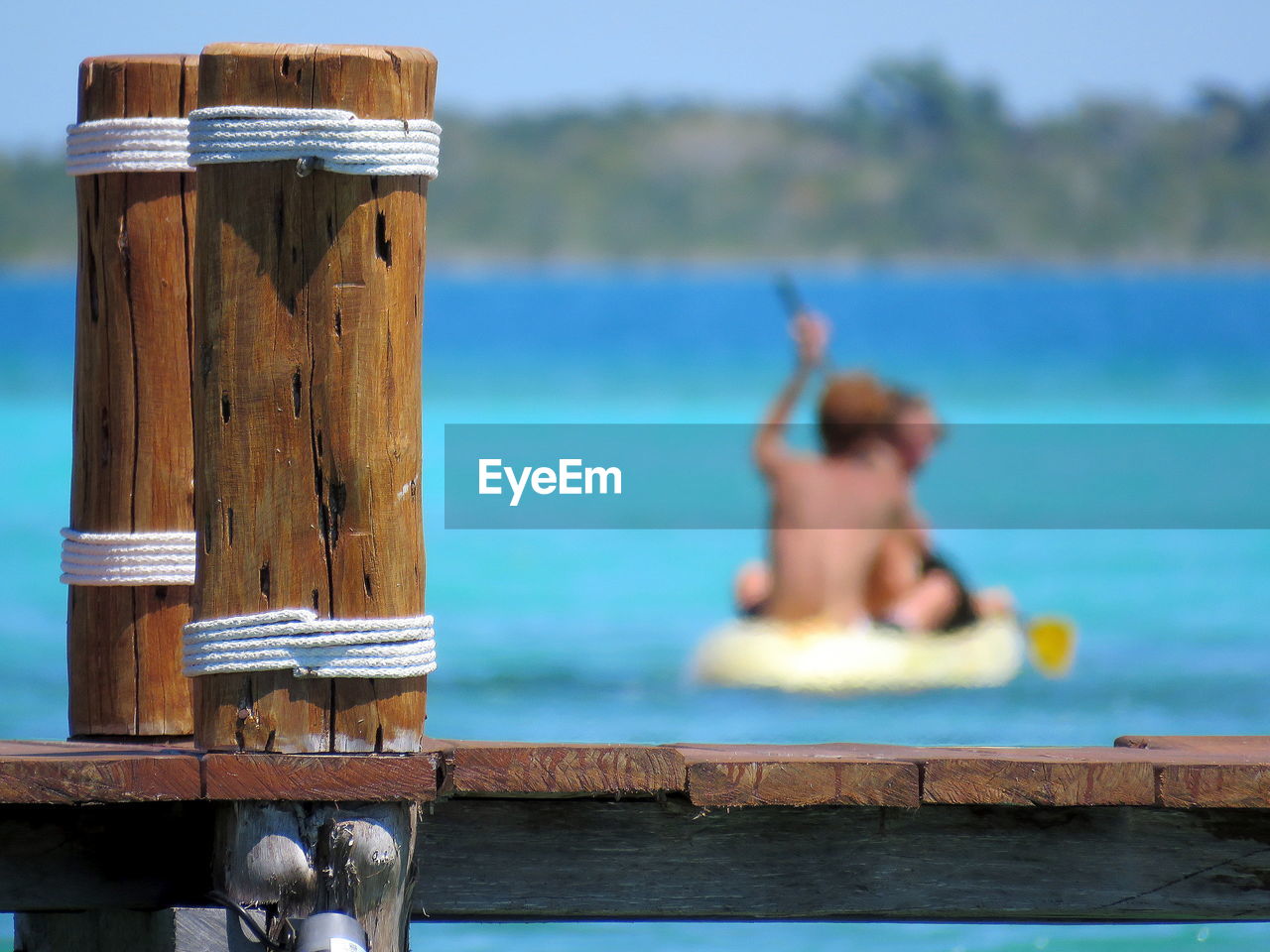 Close-up pier with people in a canoe in background