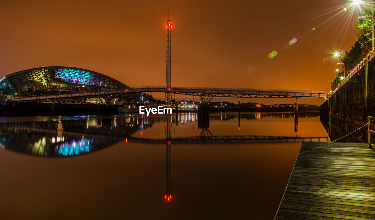 Bridge over clyde river by modern building against sky at night