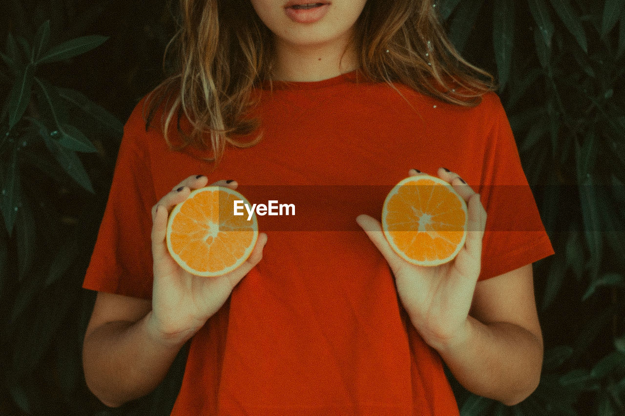 Midsection of woman holding orange slices by plants