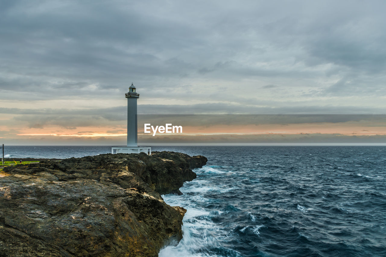 Lighthouse by sea against sky during sunset