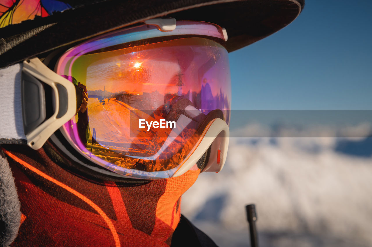 Ski goggles with reflection of snow-capped mountains. a man on a ski slope stands in profile and