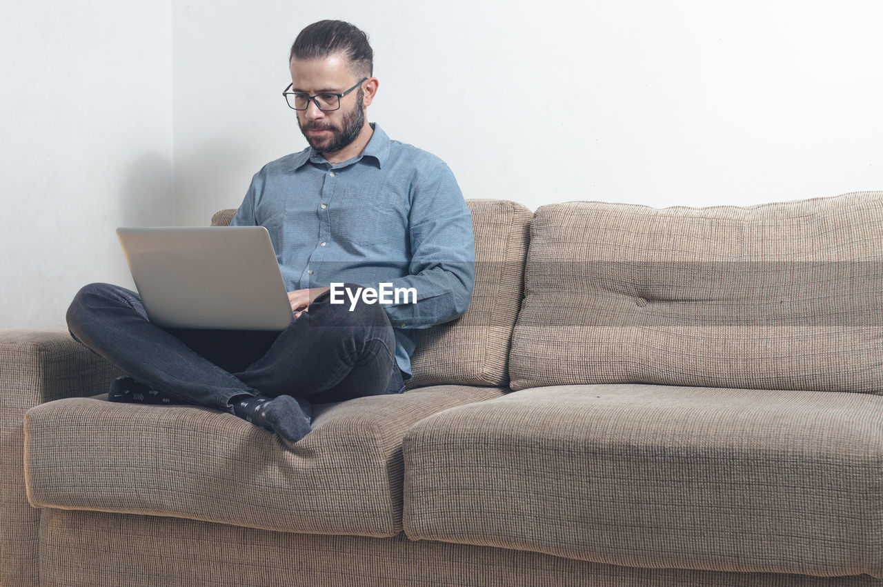 Full length of man using laptop while sitting on sofa at home