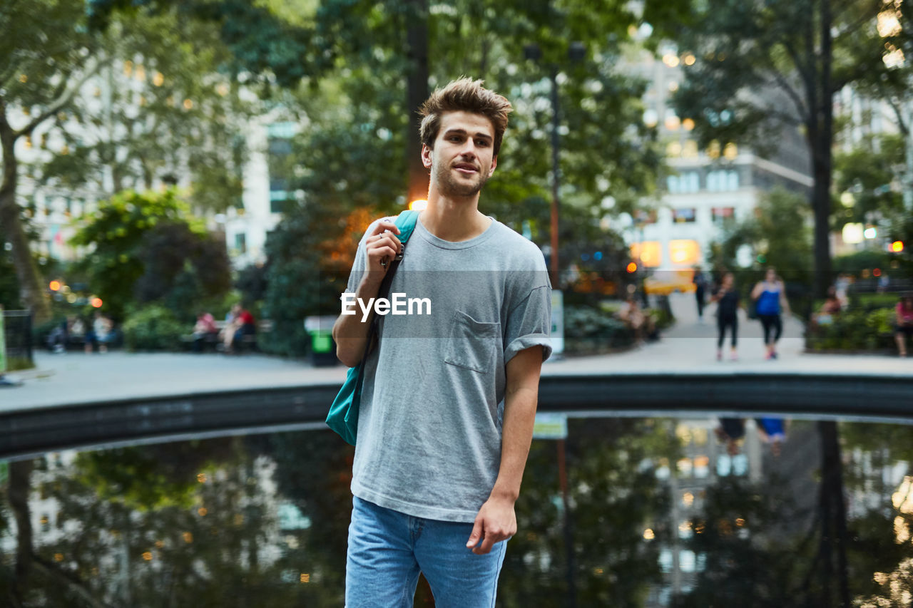 Young man standing by pond in city