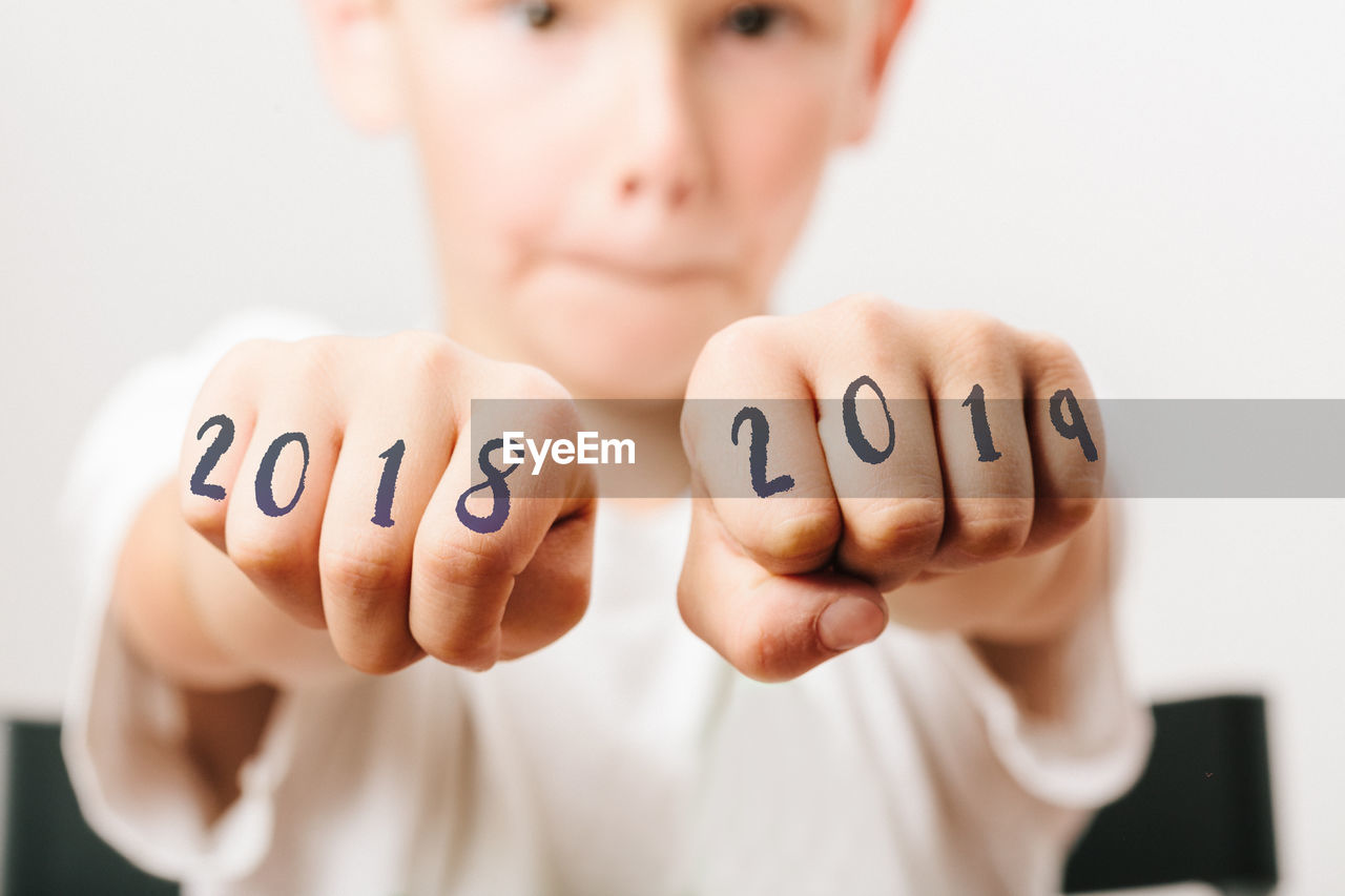Close-up portrait of boy showing numbers on fists at home