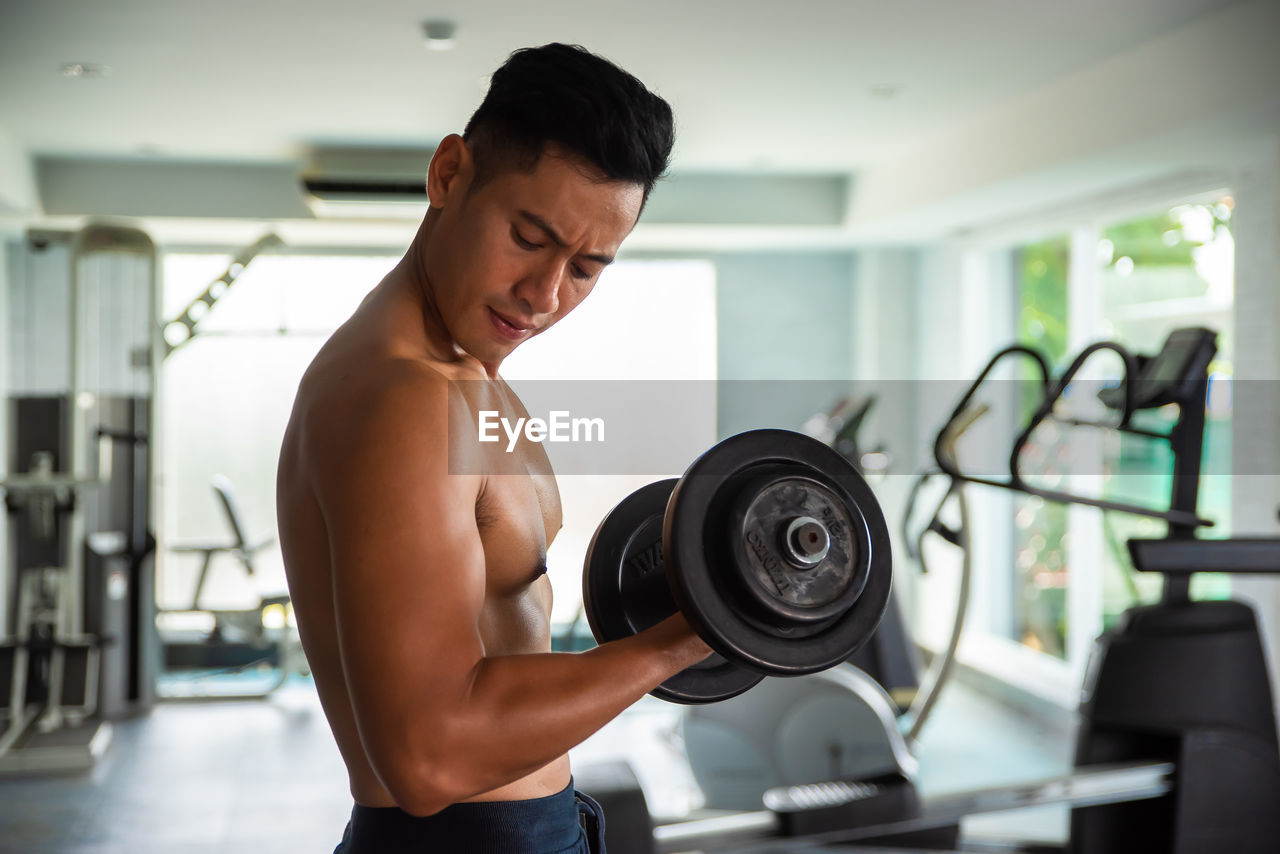 MIDSECTION OF SHIRTLESS MAN STANDING IN BUILDING