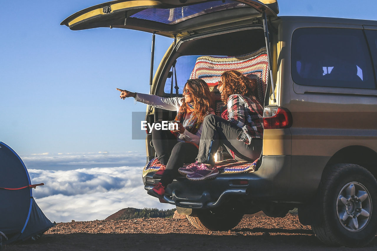 Friends talking while having coffee in car trunk