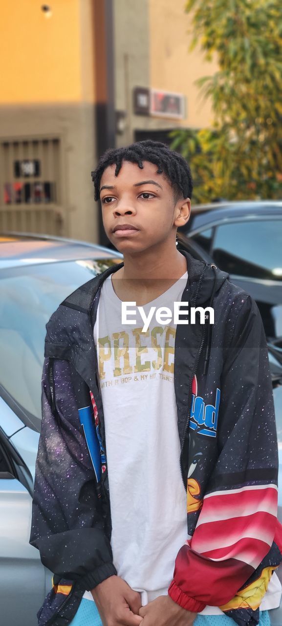 Side view of young man standing by cars