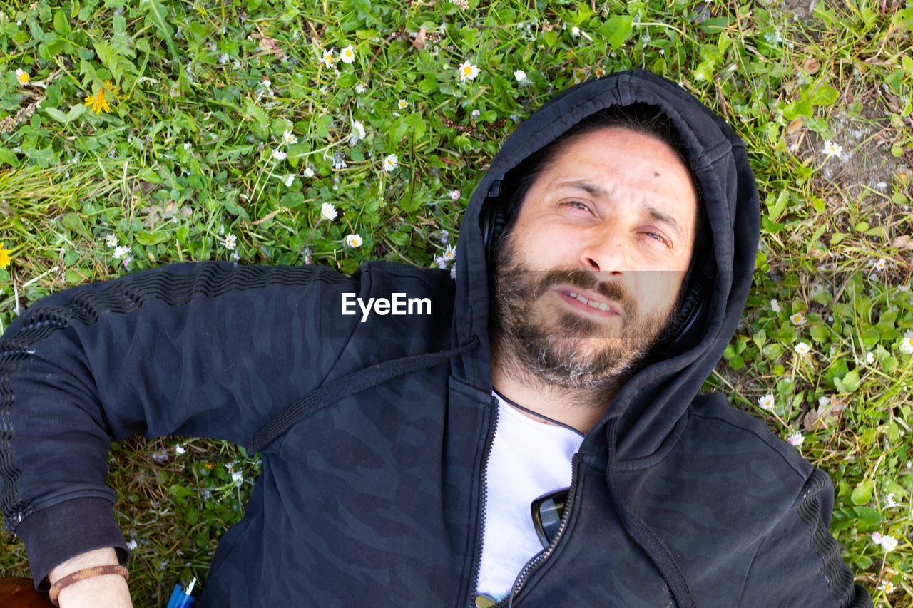 Hippy man lying down with beard and headphones outdoors on the grass