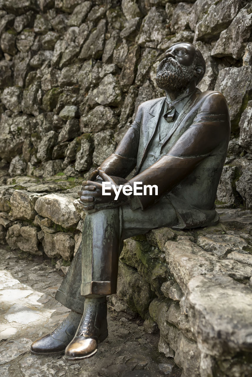 MAN SITTING ON ROCK AGAINST STONE WALL