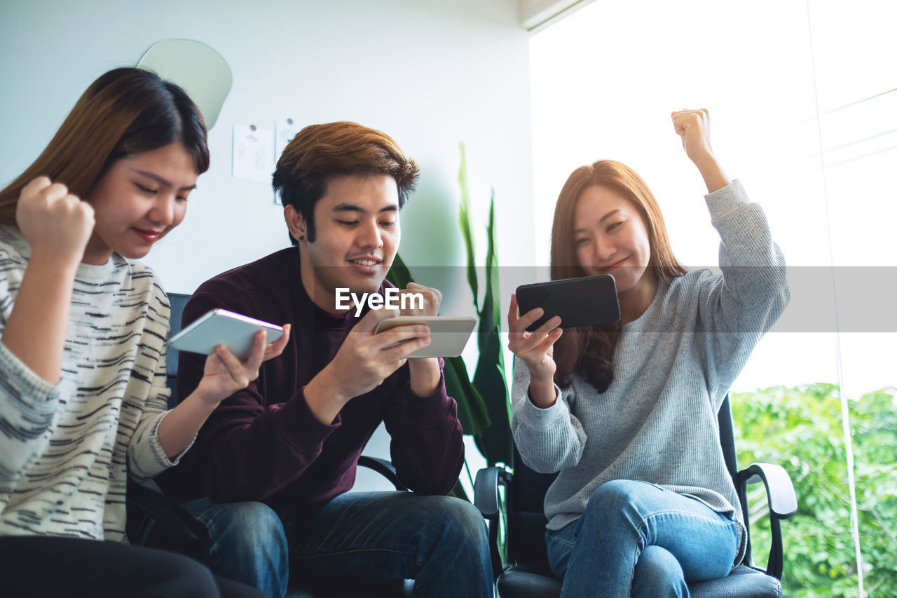 technology, communication, wireless technology, group of people, adult, smartphone, portable information device, women, sitting, togetherness, mobile phone, conversation, happiness, friendship, smiling, young adult, indoors, emotion, relaxation, lifestyles, person, activity, men, casual clothing, cheerful, female, holding, teenager, sofa, enjoyment, fun, telephone, selfie, youth, small group of people, three quarter length, bonding, looking, digital tablet, leisure activity, child, internet, living room, portability, domestic room, positive emotion, laughing, clothing, social group, human face, furniture, computer network, youth culture
