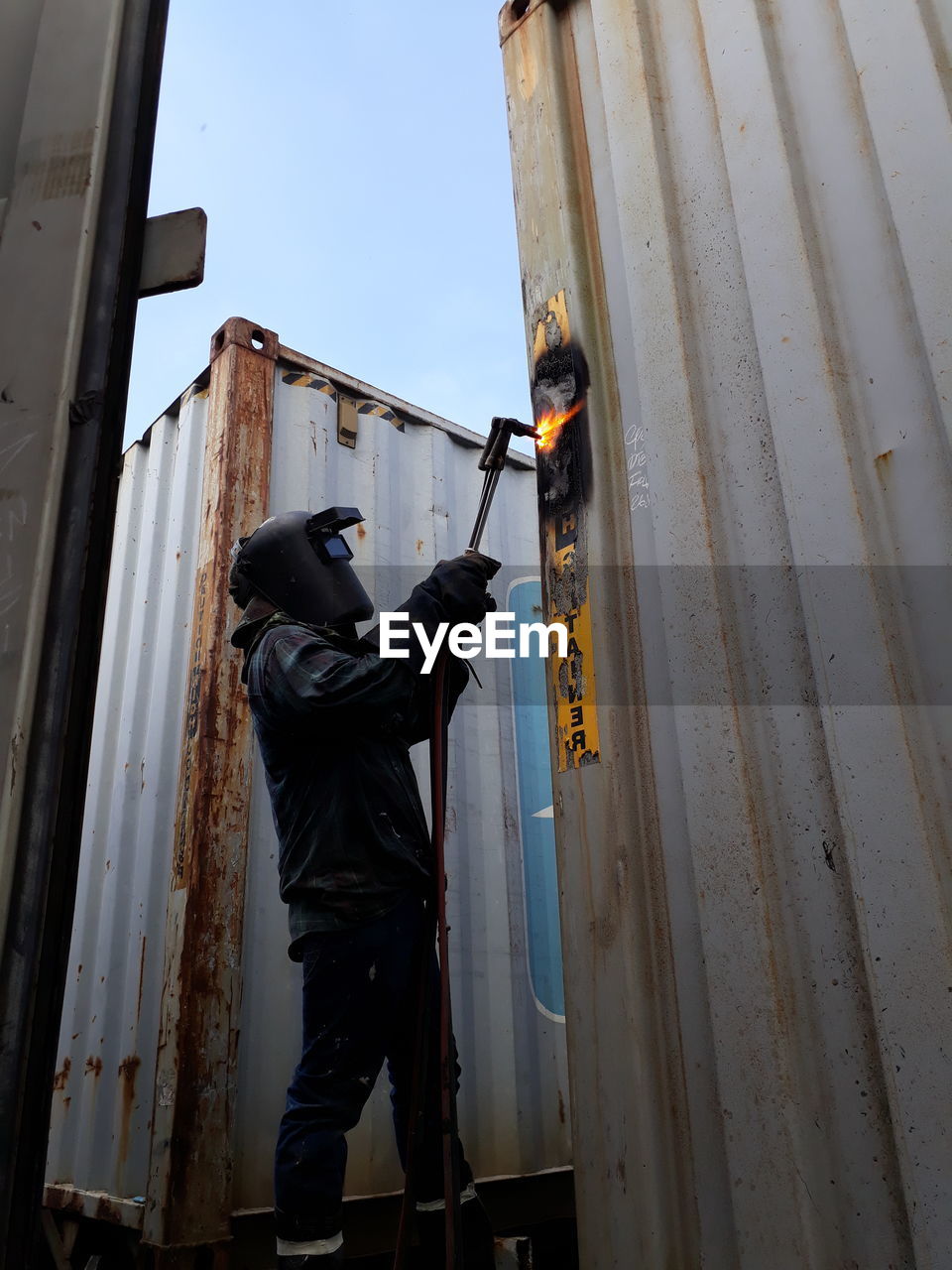 LOW ANGLE VIEW OF MAN WORKING ON METAL BUILDING