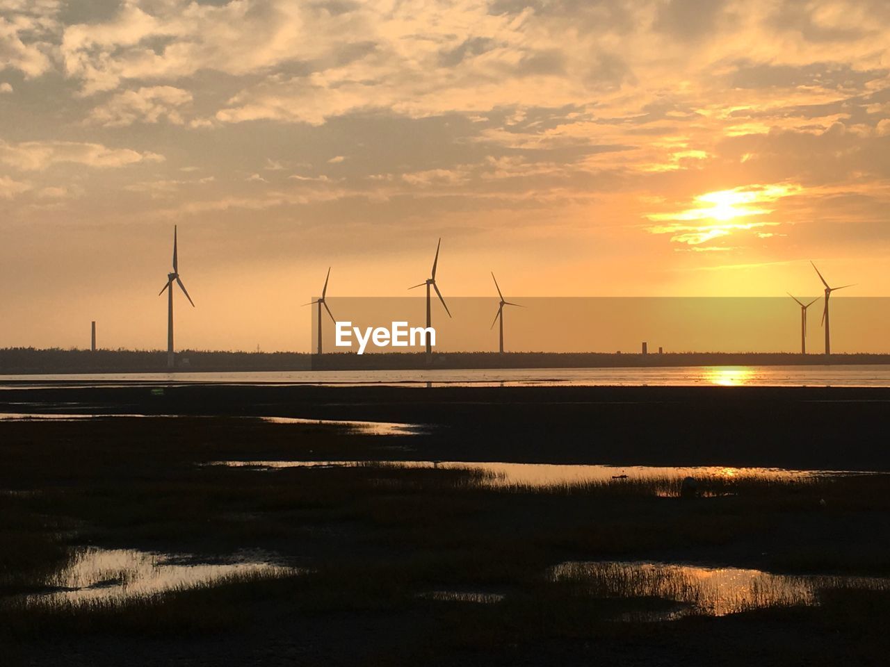 Windmills by lake against sky during sunset