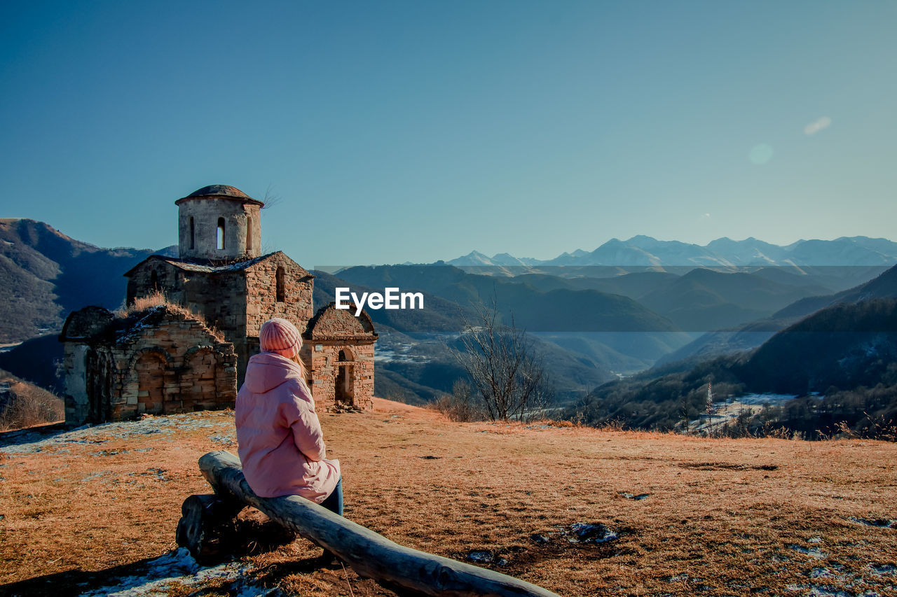 Woman sitting on mountain against sky