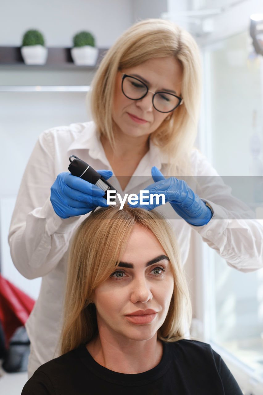 Doctor examines head skin of young woman with special dermatology equipment system, hairloss and