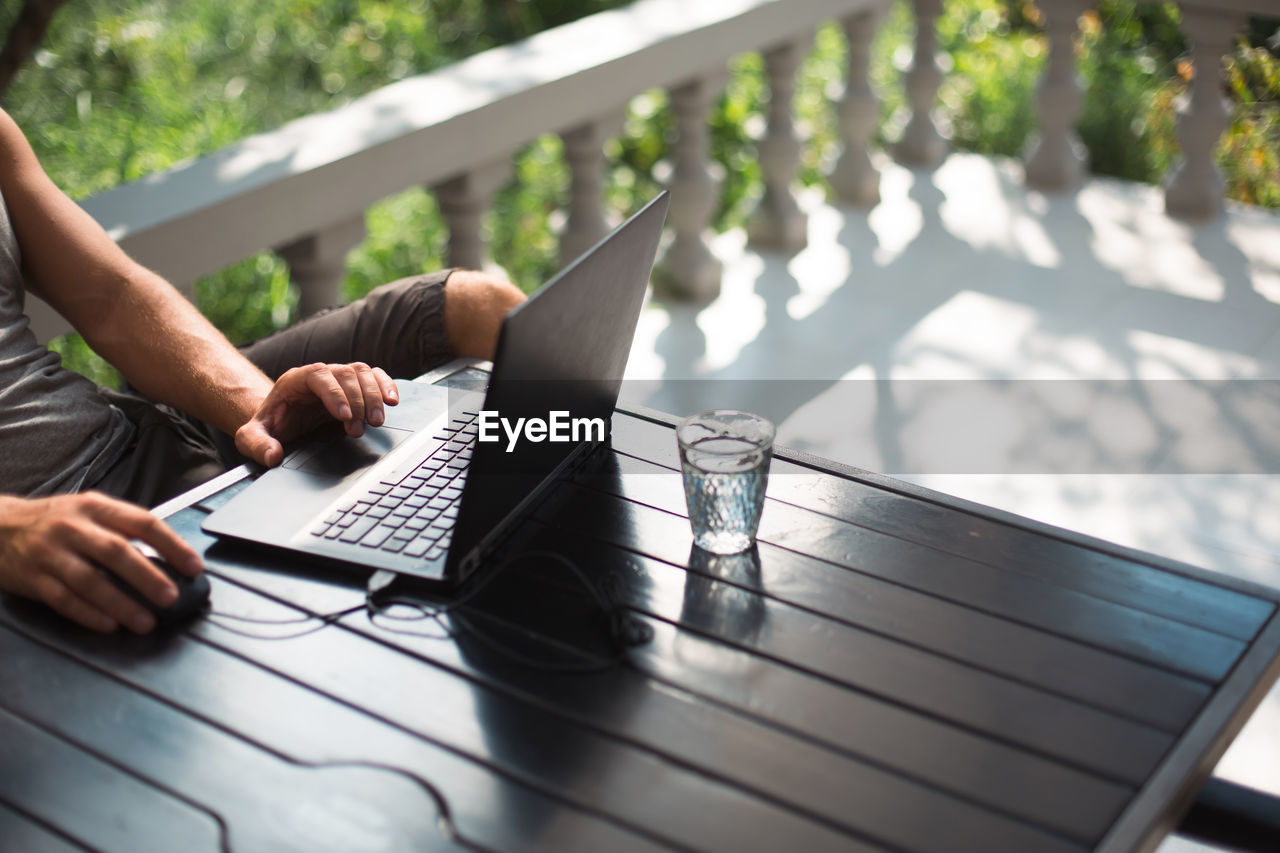 midsection of man using laptop while sitting on wooden table