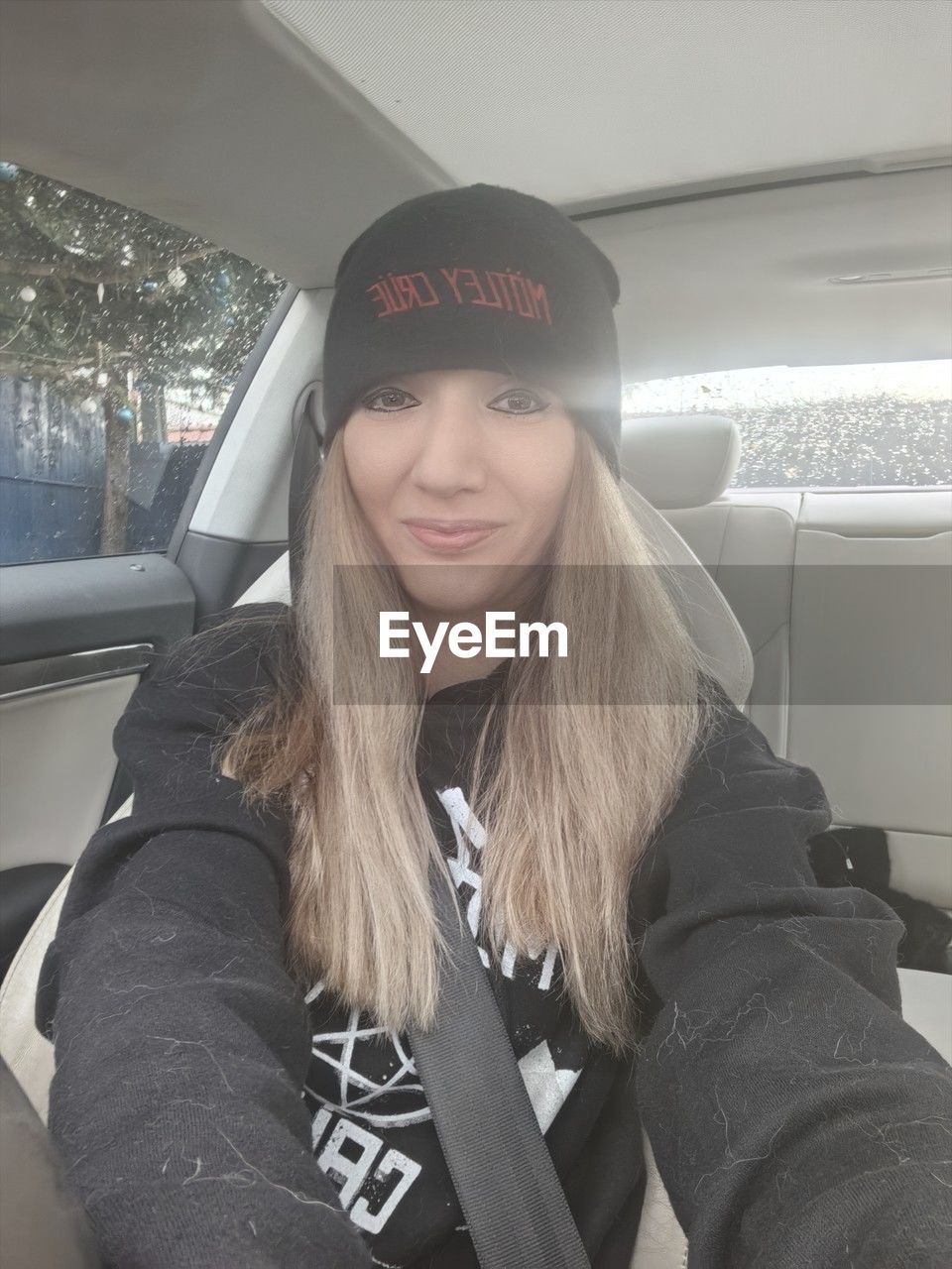 transportation, mode of transportation, one person, vehicle interior, car, portrait, motor vehicle, women, travel, clothing, smiling, adult, long hair, young adult, looking at camera, cap, fashion accessory, hairstyle, lifestyles, car interior, front view, winter, hat, sitting, person, happiness, journey, day, blond hair, human face, indoors, emotion, land vehicle, glasses, vehicle, waist up, leisure activity, warm clothing, casual clothing, human hair, fashion, knit hat