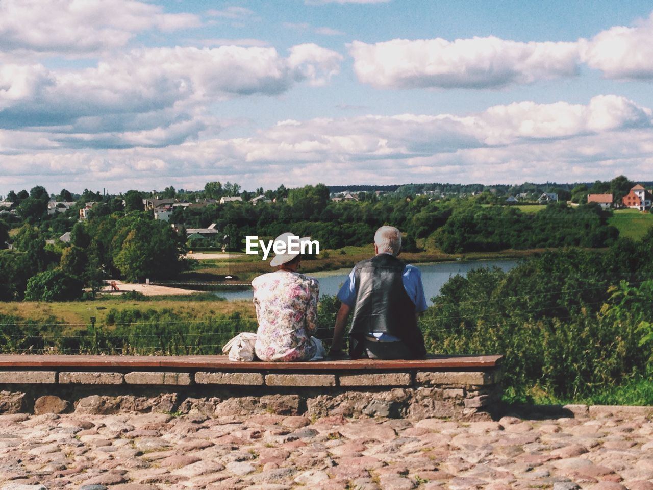 Rear view of senior couple sitting on bench against sky at park