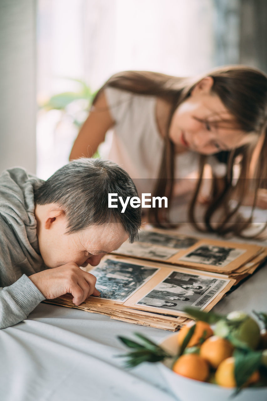 Unforgettable moments, little girl and elderly woman with down syndrome cherish family album viewing