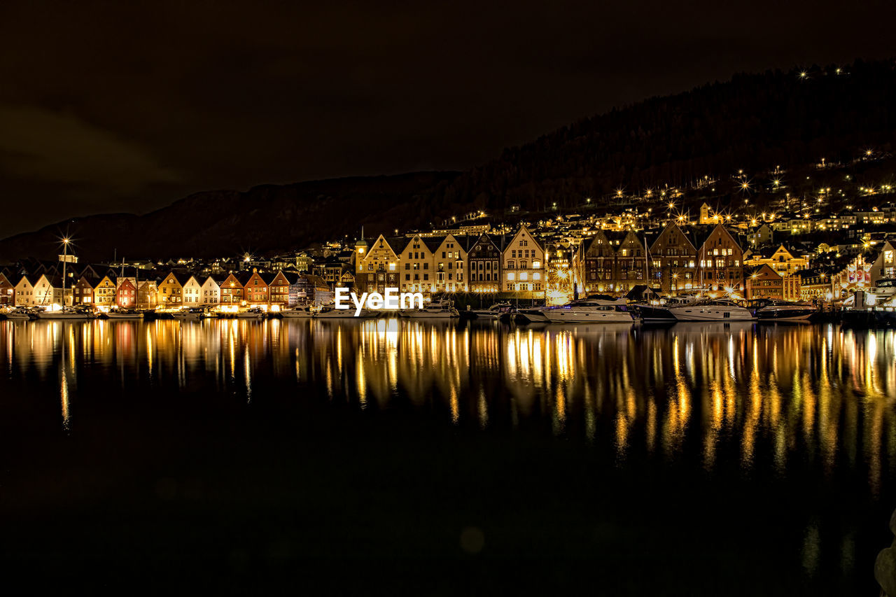 Illuminated buildings by lake against sky at night