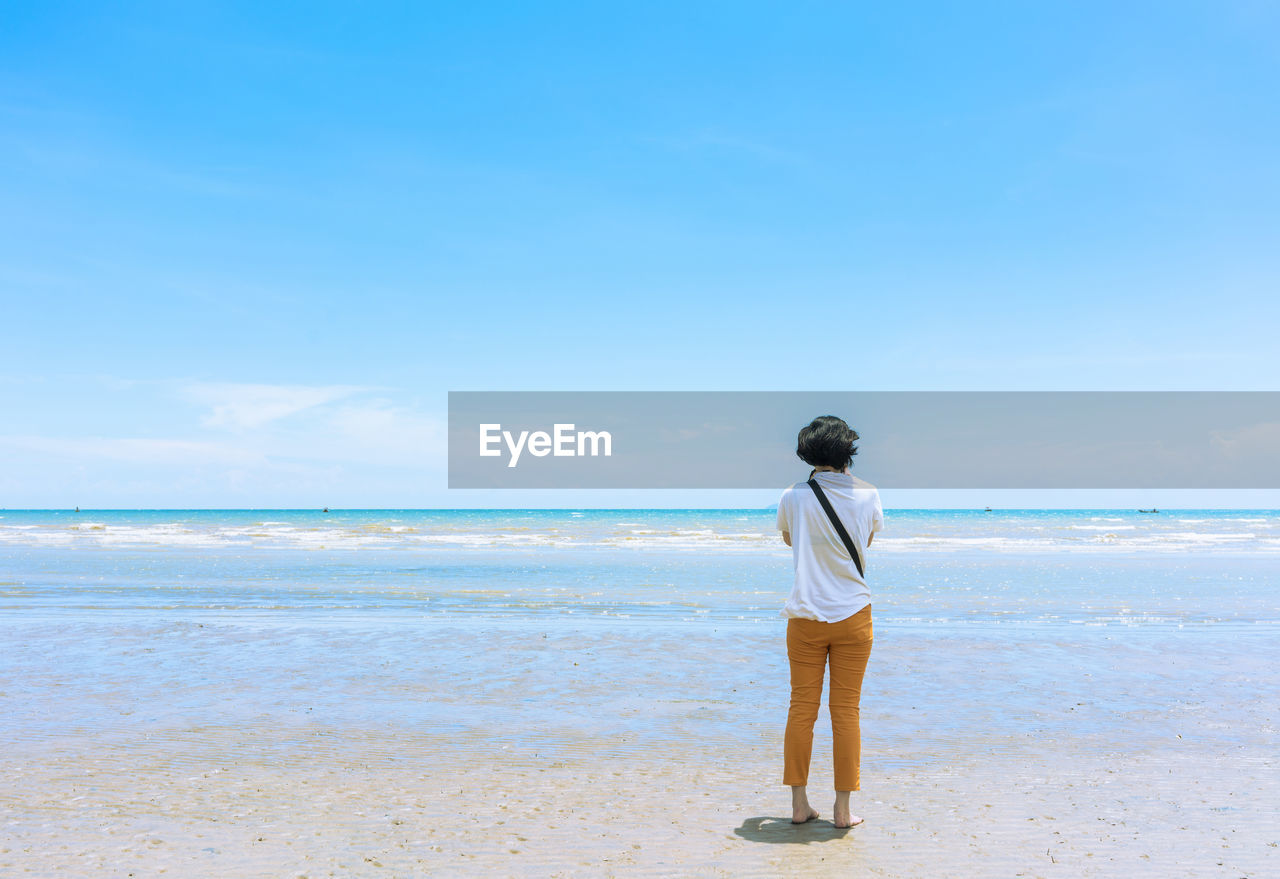 Rear view of woman standing at beach against blue sky