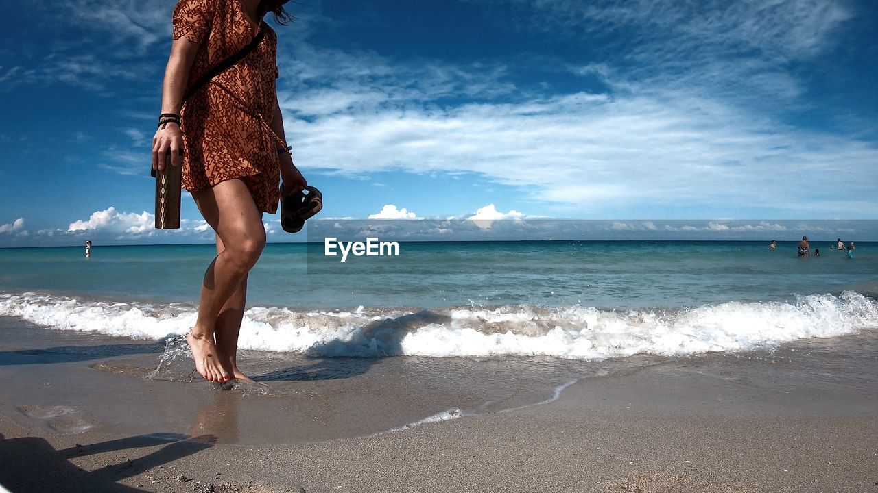 WOMAN STANDING ON BEACH AGAINST SEA