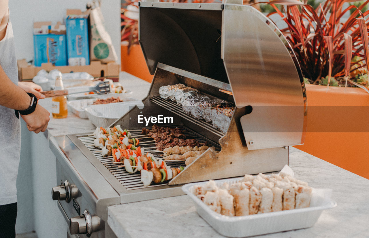 Midsection of man preparing food on barbeque grill at table