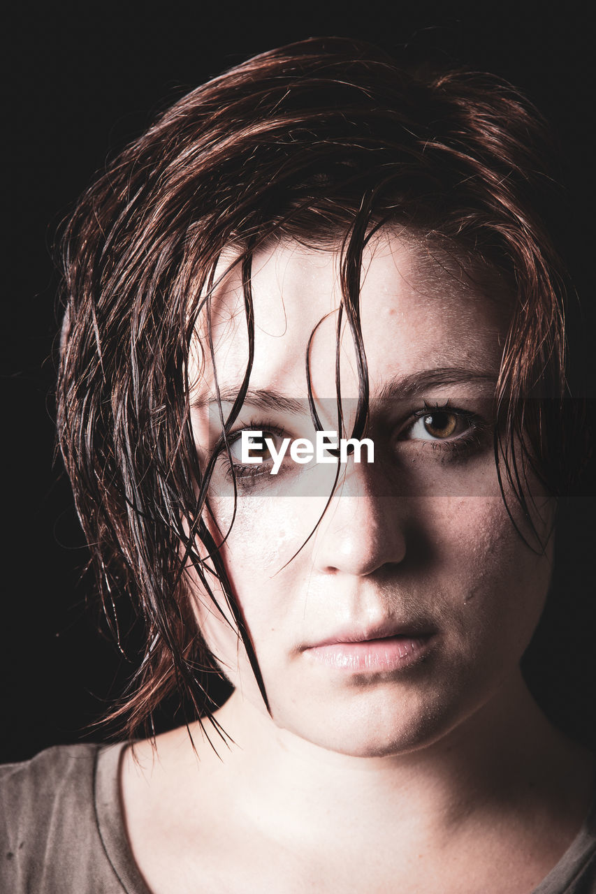 Close-up portrait of young woman against black background