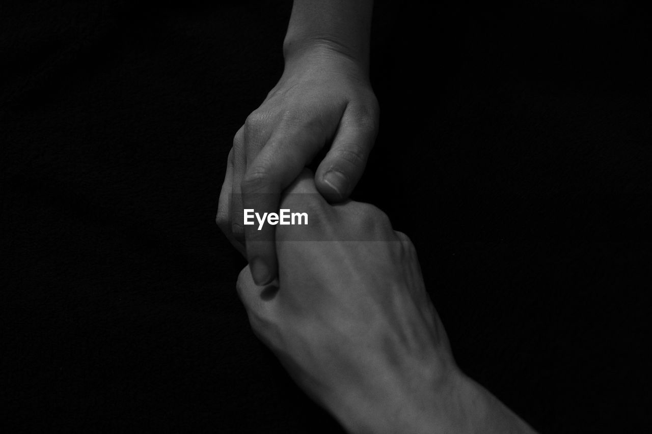 Cropped image of people holding hands against black background