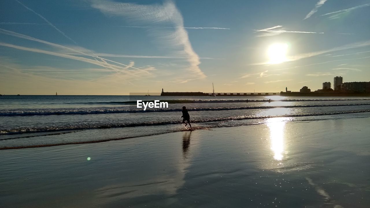 Silhouette boy running on beach against sky during sunset