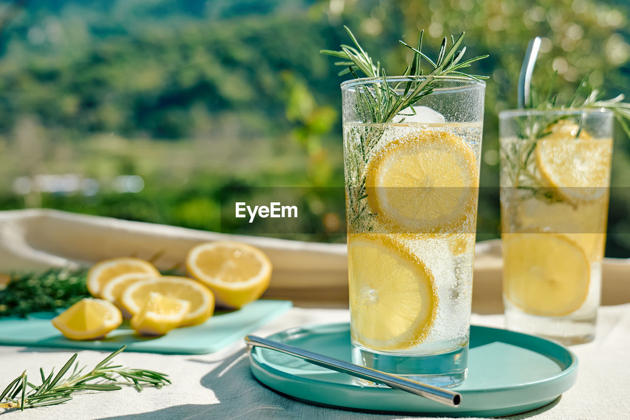 Summer refreshing lemonade drink or alcoholic cocktail with ice, rosemary and lemon slices on table