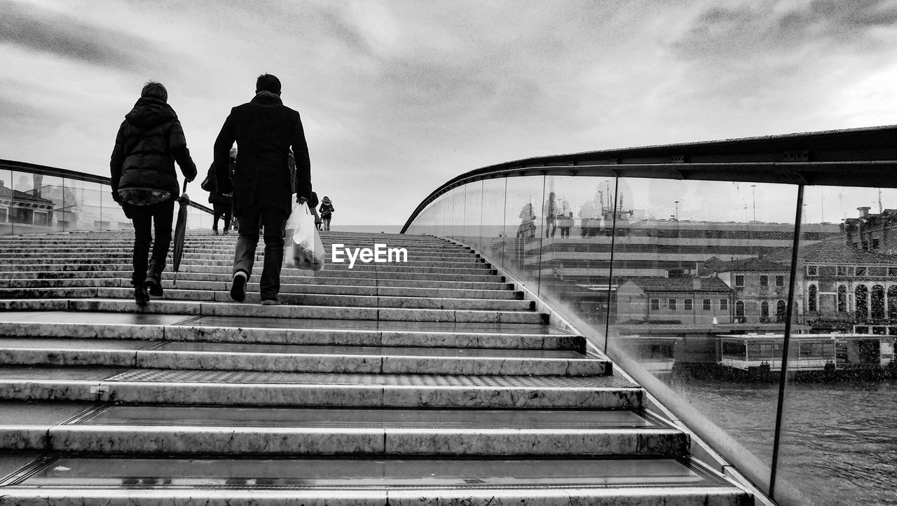 Rear view of people on steps at bridge over river