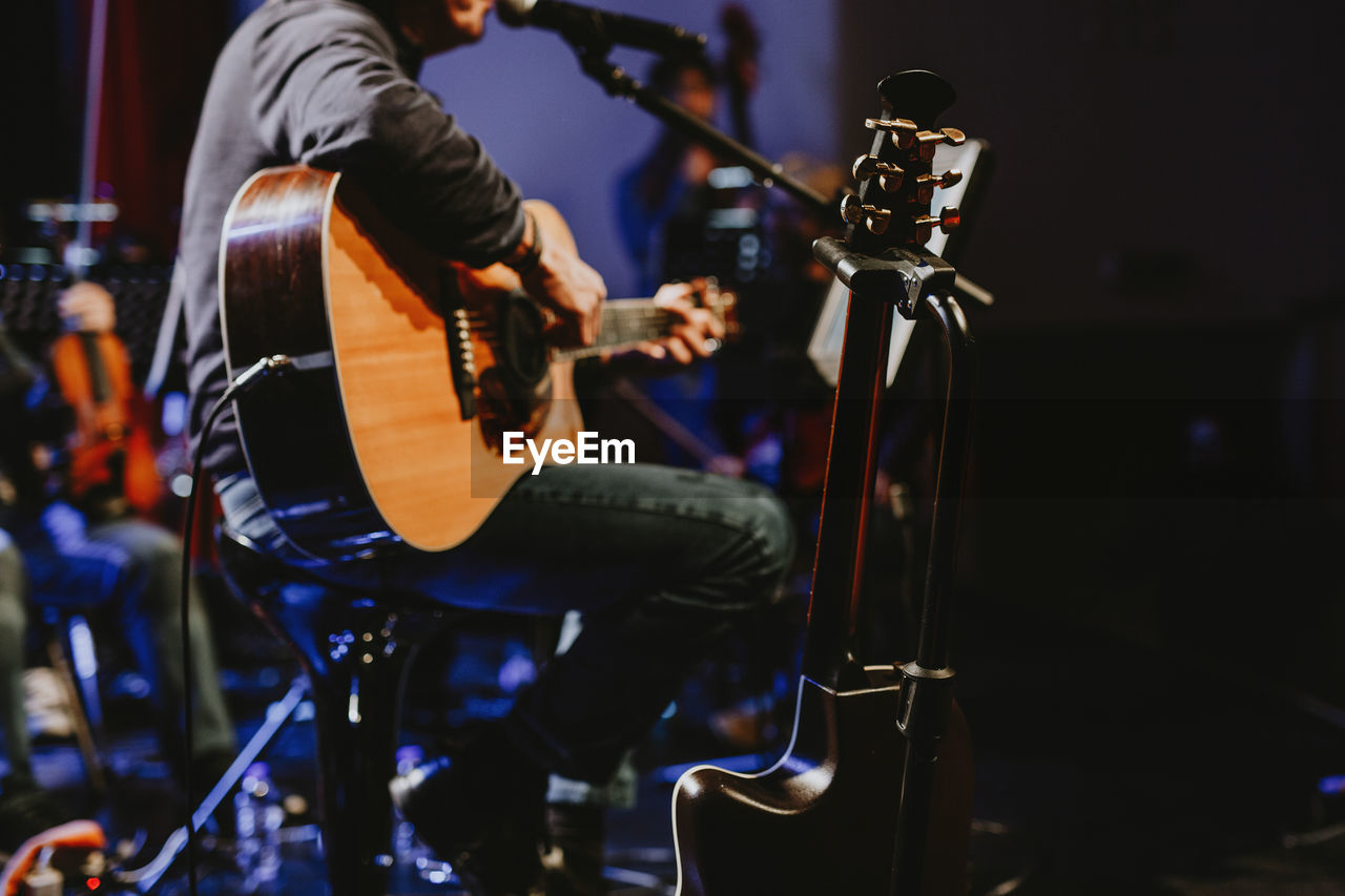 Midsection of man playing guitar at music concert