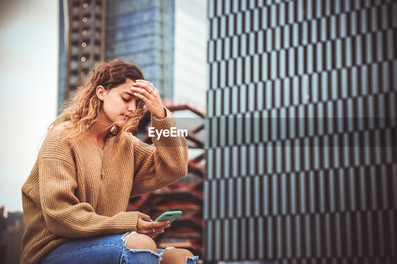 Woman using mobile phone while sitting by building