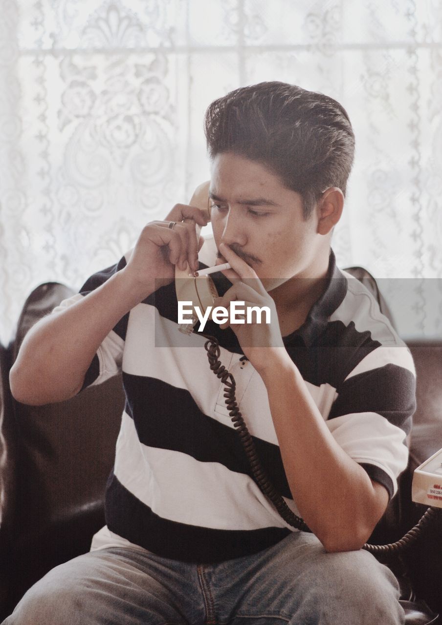 Man smoking cigarette while talking on phone at home